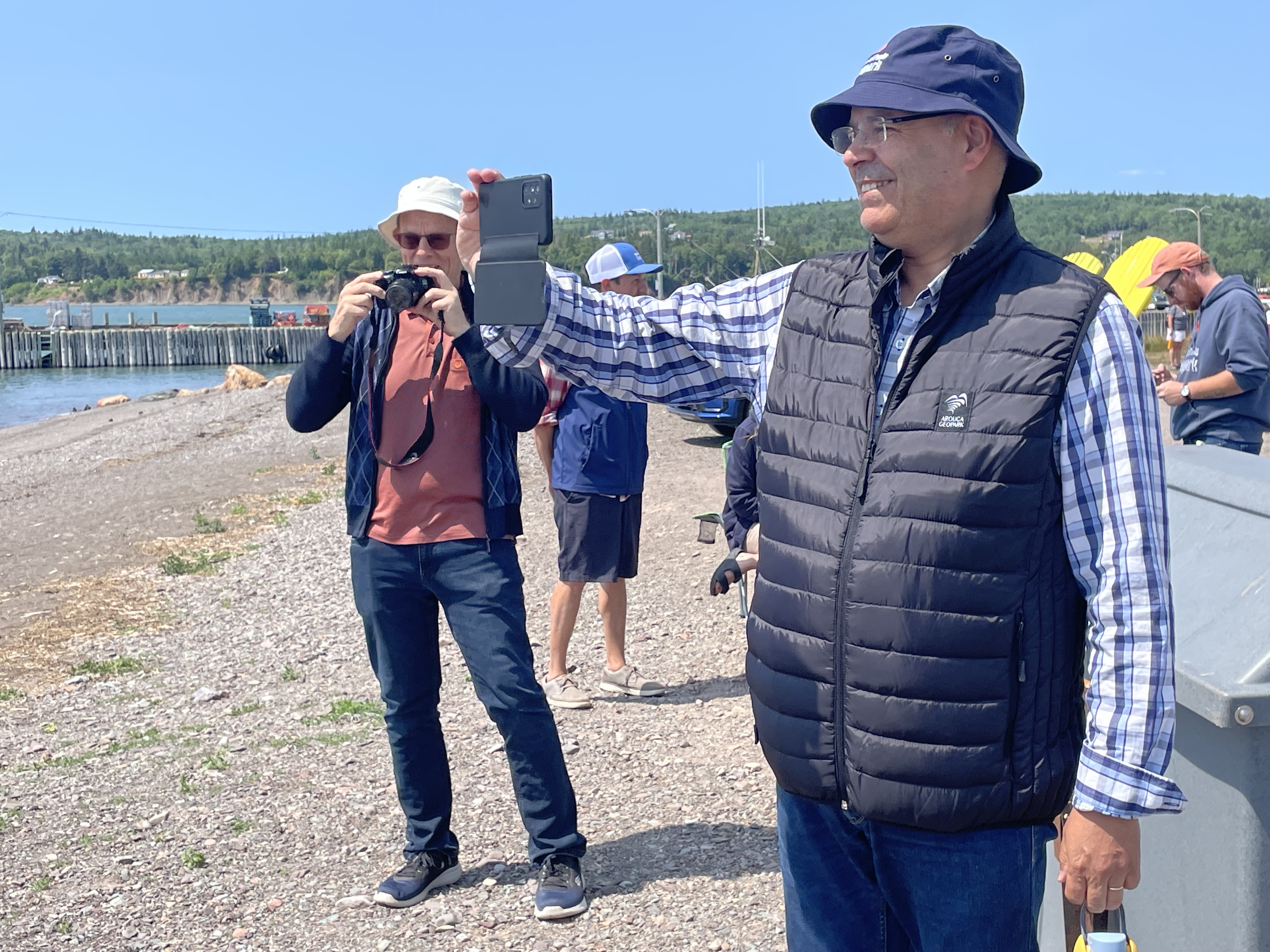 Two men stand on a beach with cameras.