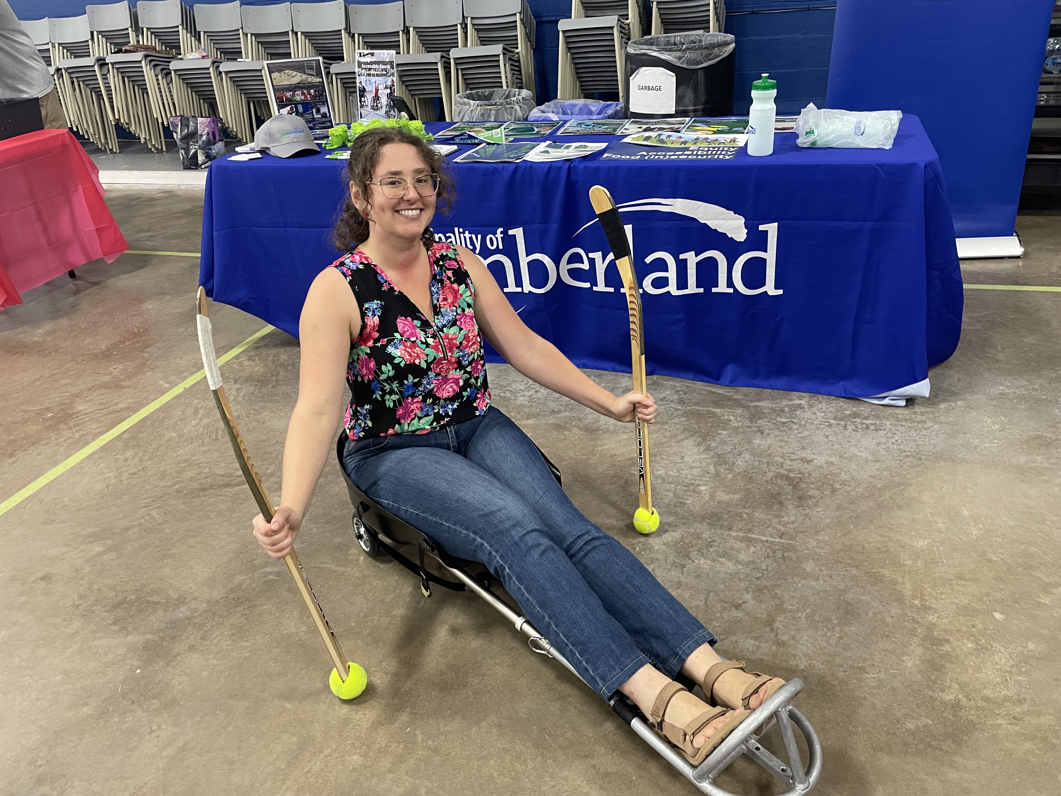 A woman sits in an accessible sled while holding two short sticks.
