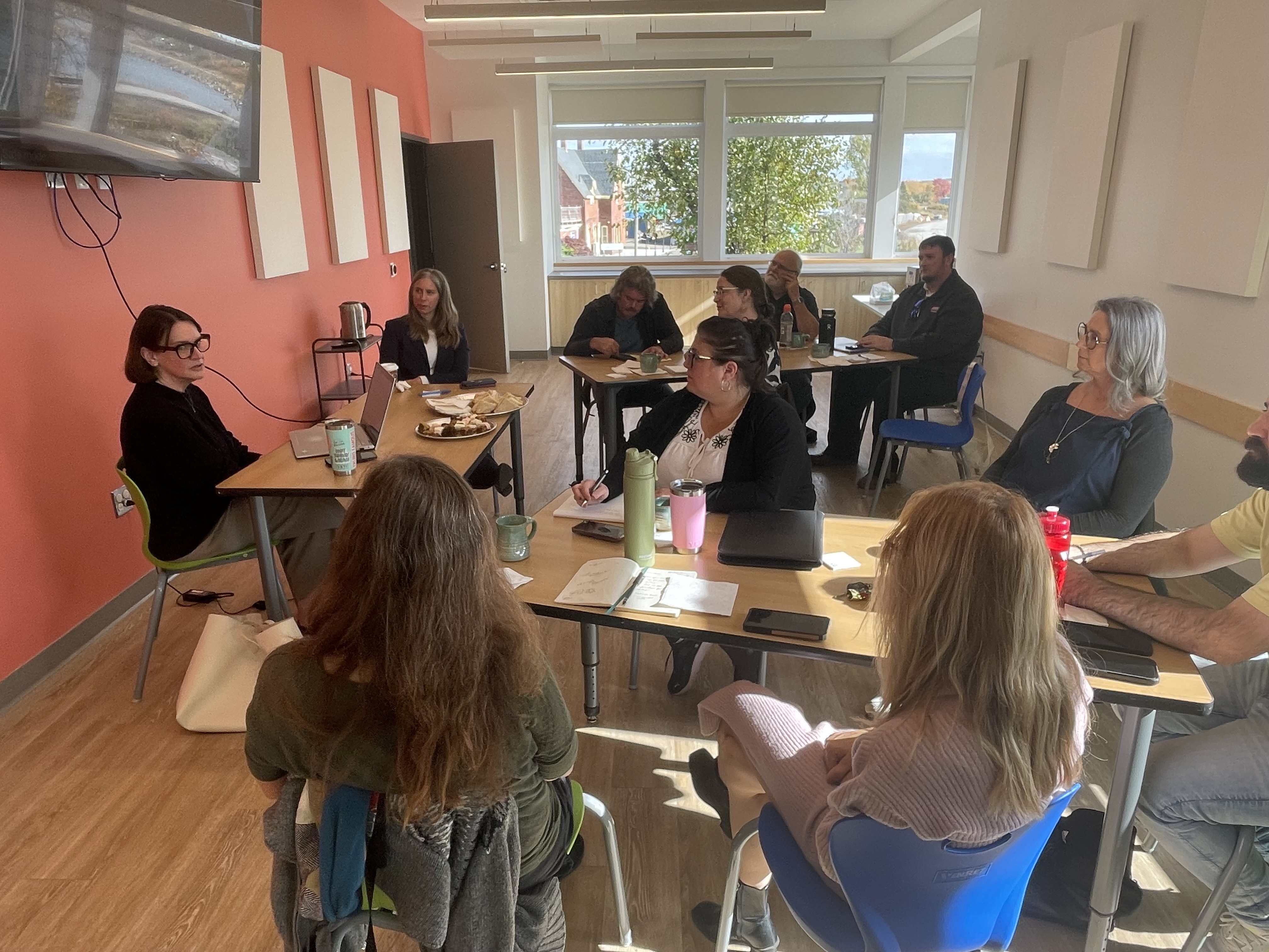A group of nine people sit around tables while a lead presenter at the front talks about marketing small business